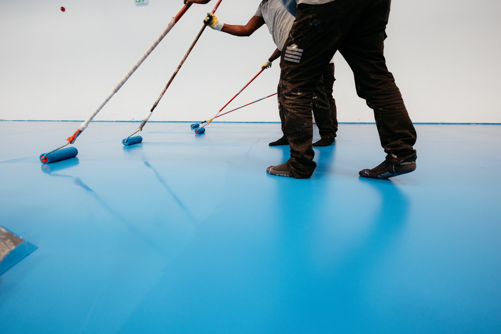 Construction workers painting a blue epoxy resin floor in a sports hall