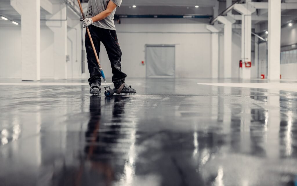 Worker applying black epoxy resin in a big open empty warehouse