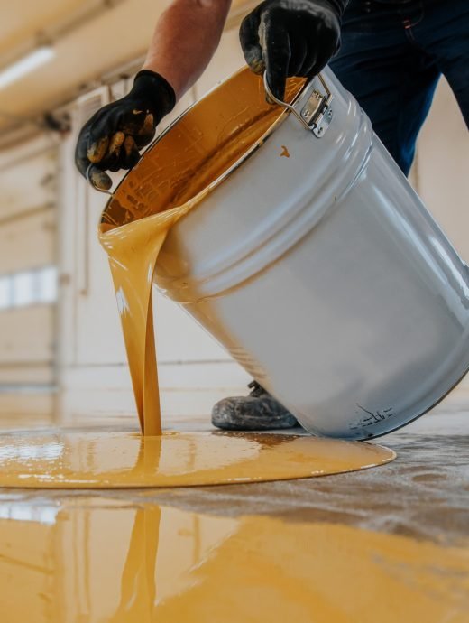 Closeup shot of a construction worker pouring out epoxy resin from a bucket onto a floor Closeup shot of a construction worker pouring out epoxy resin from a bucket onto a floor